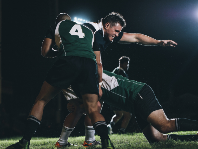 A rugby player in a night match being tackled by two opponents.