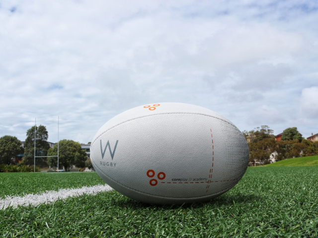 A white rugby ball sitting on a green grass field with a cloudy sky in the background.