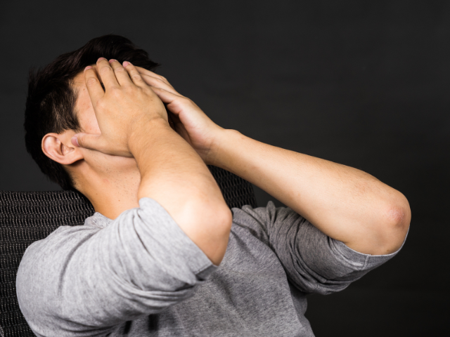 A man sitting with his hands covering his face, appearing frustrated.