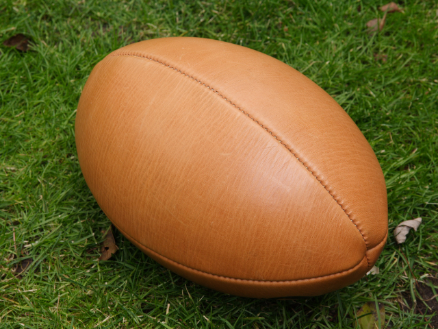 A vintage leather rugby ball on a grass surface.