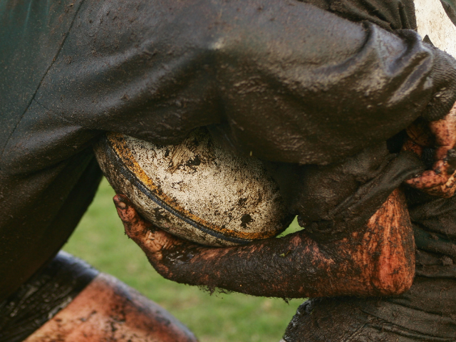 Close-up of two rugby players tightly gripping a ball covered in mud during a match.