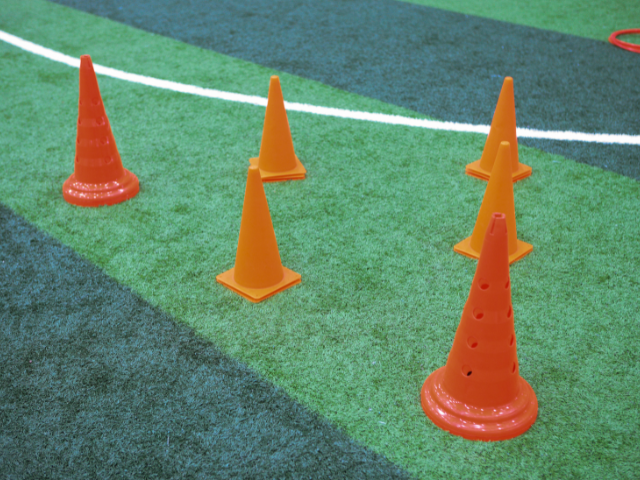 Orange rugby cones arranged in a formation on artificial turf, ready for a practice session.